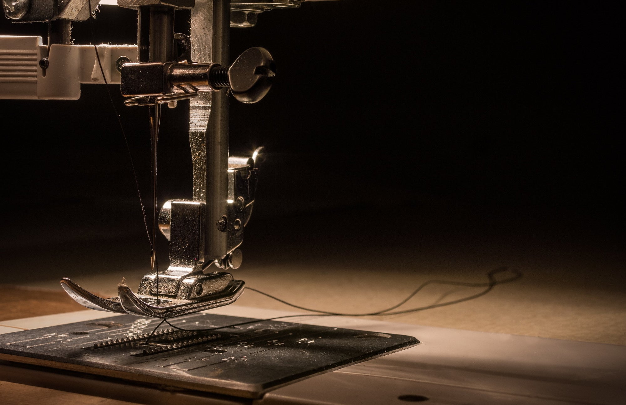 Close-up of a sewing machine needle and foot on a wooden surface.