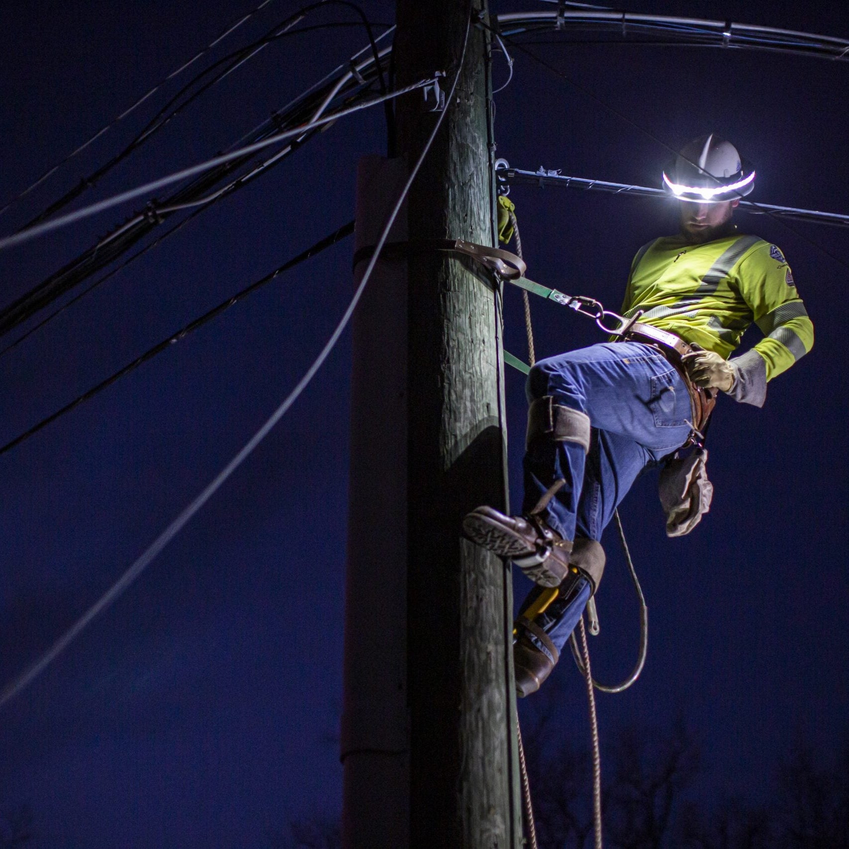 Person working on a power pole at night with safety gear
